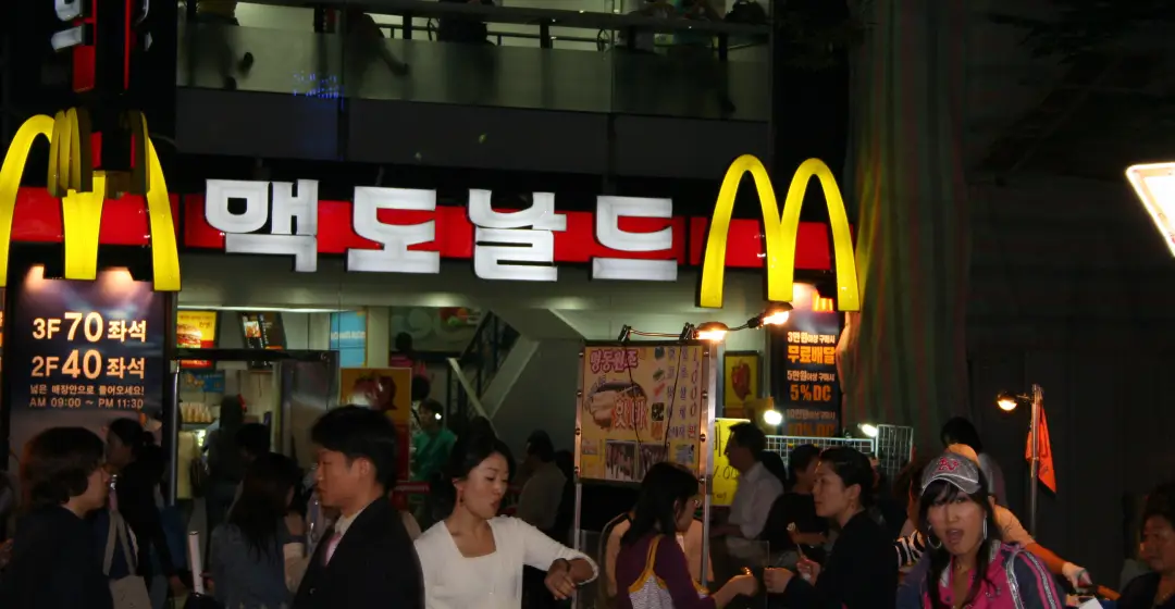 McDonald’s exterior signage and golden arches at night with busy crowd and Korean text storefront.