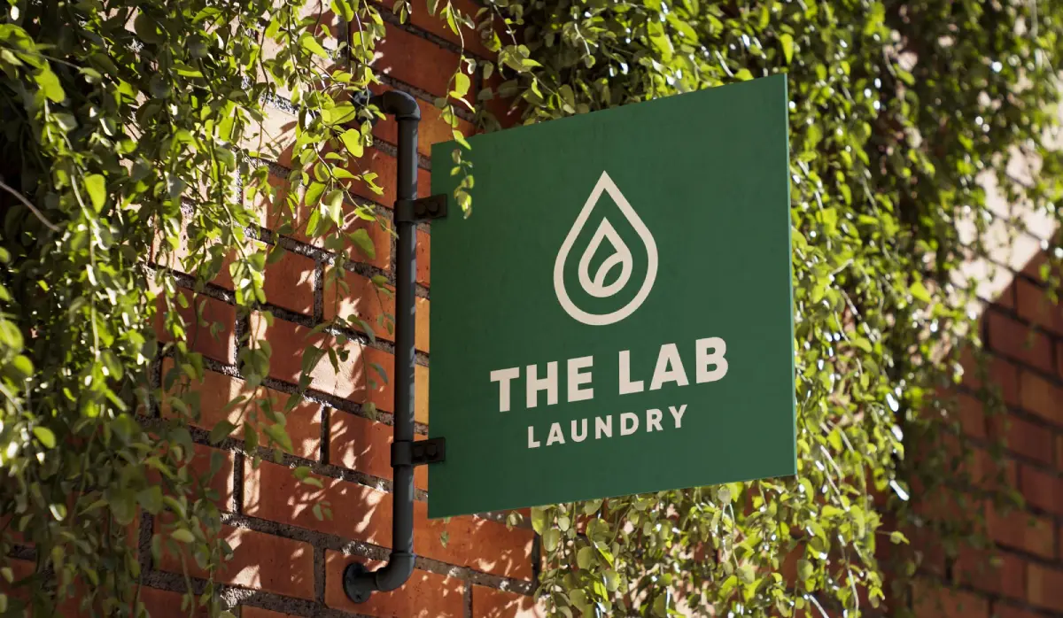 THE LAB LAUNDRY green sign with white droplet logo, modern minimalist typography on ivy-covered brick wall.