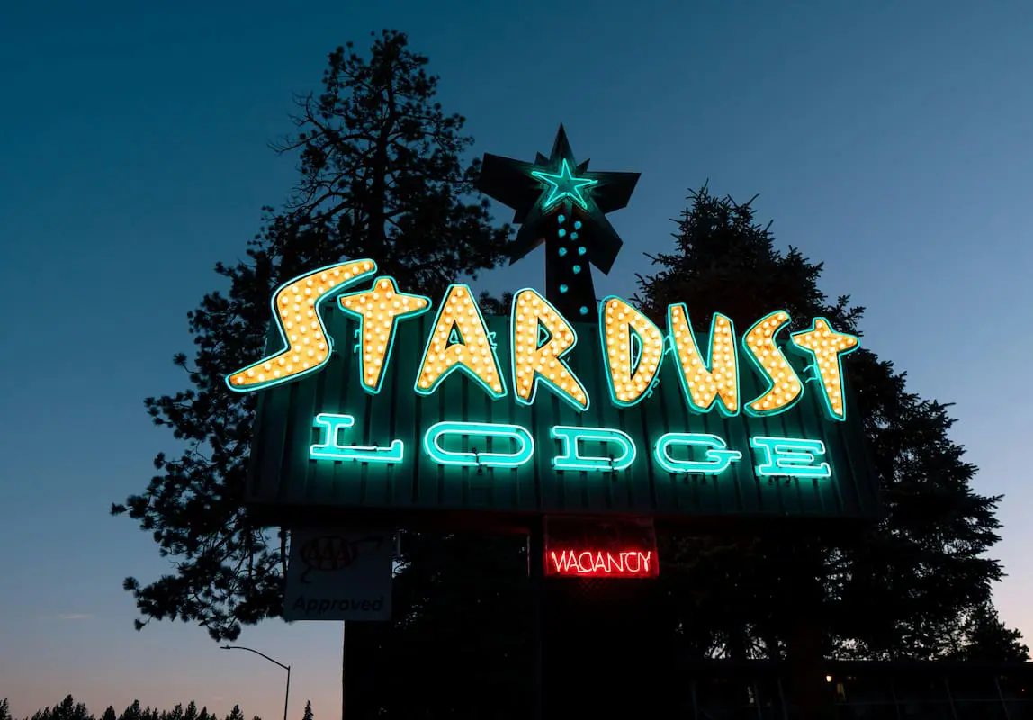 STARDUST LODGE neon sign with retro midcentury marquee styling in yellow and teal, vacancy indicator.