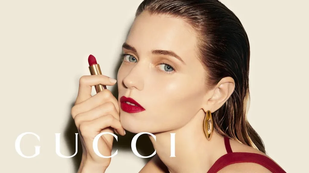 Gucci Beauty Ad Featuring A Model With Bold Red Lipstick, Sleek Hair, And Gold Hoop Earrings.