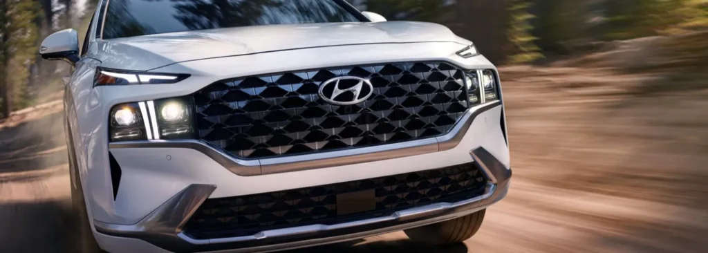 Front View Of A White Hyundai Suv With A Black Geometric Grille And Hyundai Emblem.