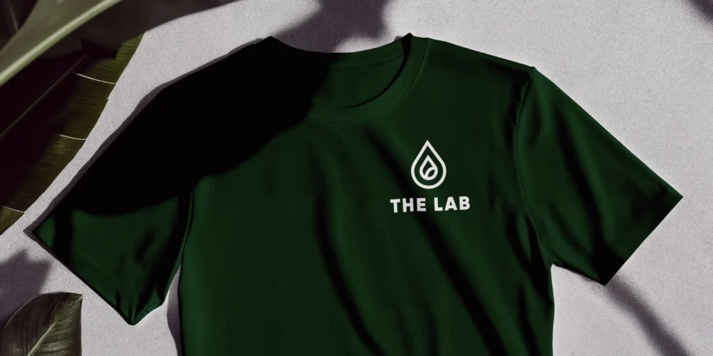 The Lab Logo On Dark Green T-Shirt With White Teardrop Emblem In Minimalist, Modern Design.