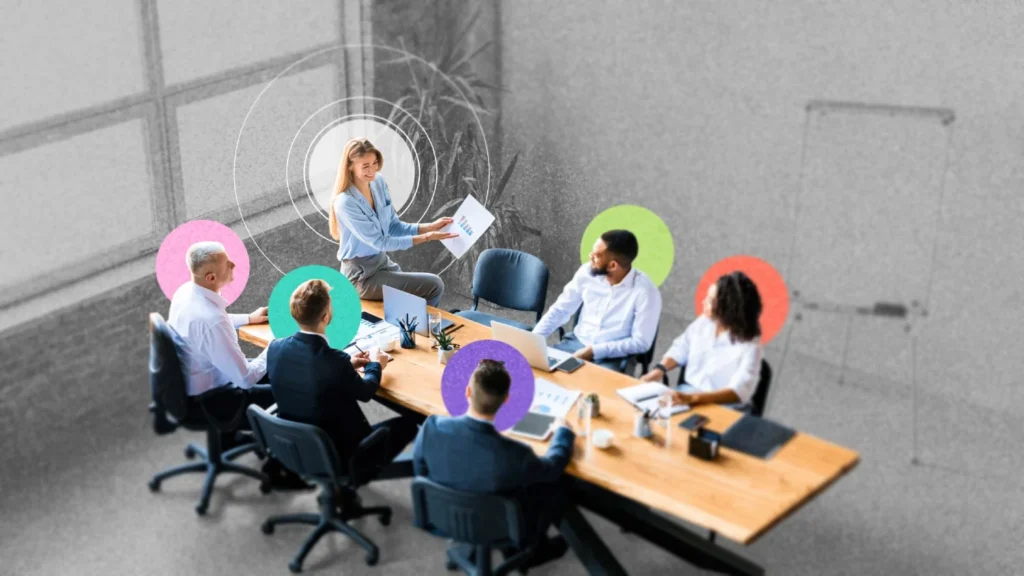 Team Presentation In A Modern Conference Room, Woman Presenting With Documents To Colleagues; Colorful Circular Overlays.
